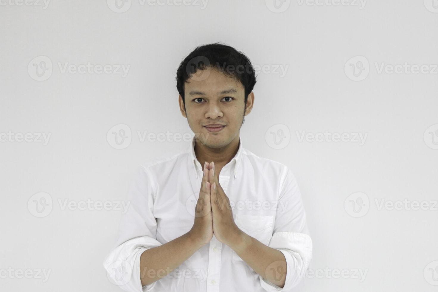 un joven asiático con camisa blanca saluda con una gran sonrisa en la cara. hombre indonesio sobre fondo gris. Eid Mubarak foto