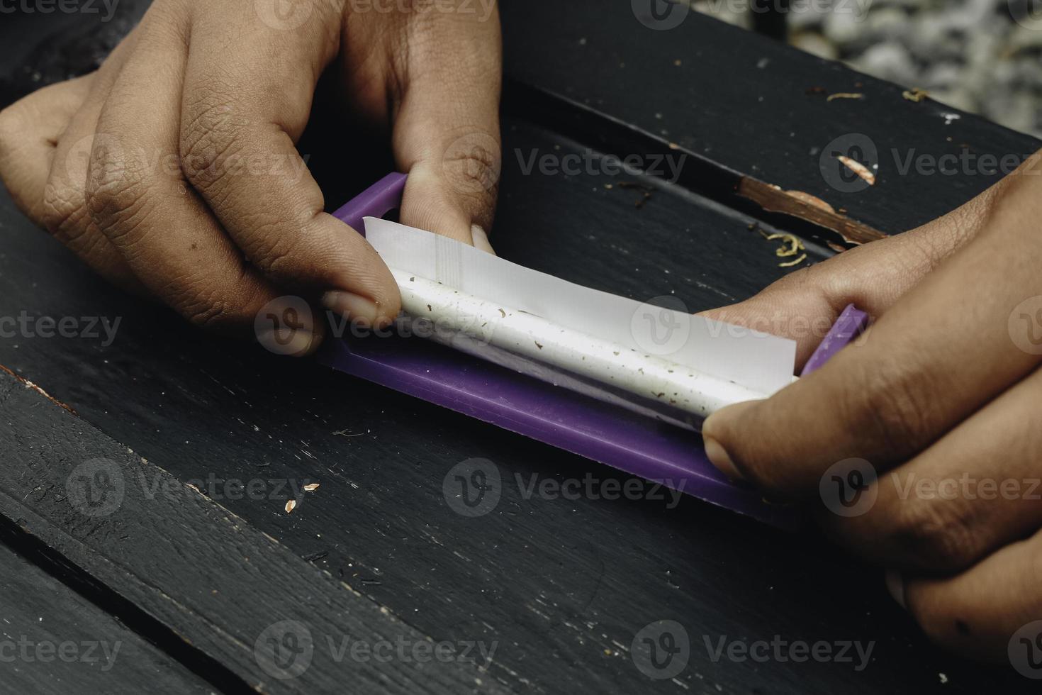Man hand makes a cigarette with rolling traditional tools, hands closeup. photo
