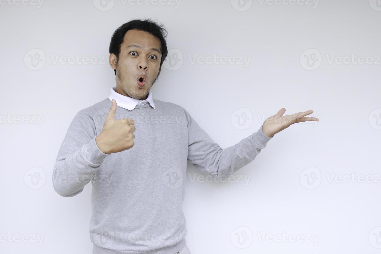 Young asian man waer white shirt is surprised and shouting wow with pointing right with his finger isolated on gray background with copy space fot your text. photo