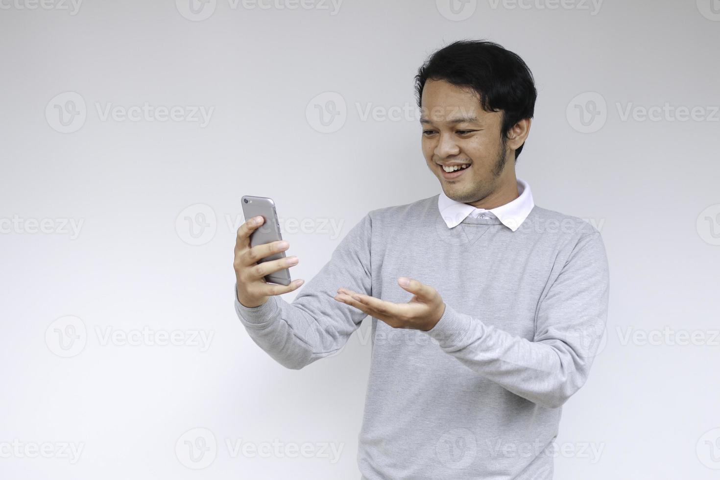 Young Asian man shocked and happy with what he see in the smartphone on isolated grey background. photo