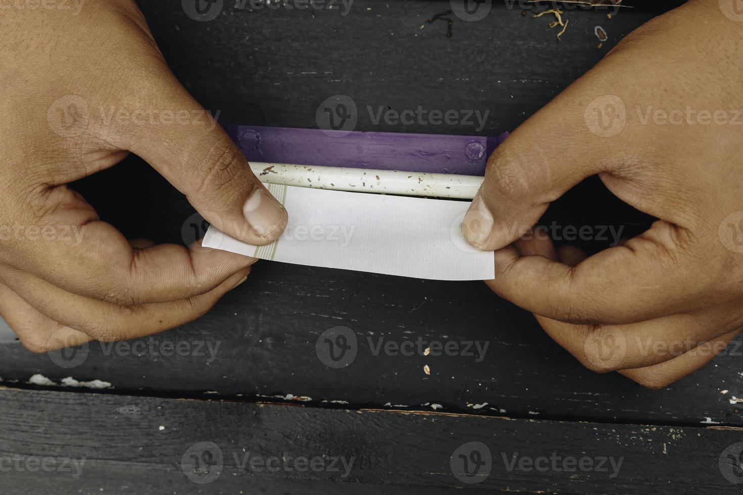 Man hand makes a cigarette with rolling traditional tools, hands closeup. photo