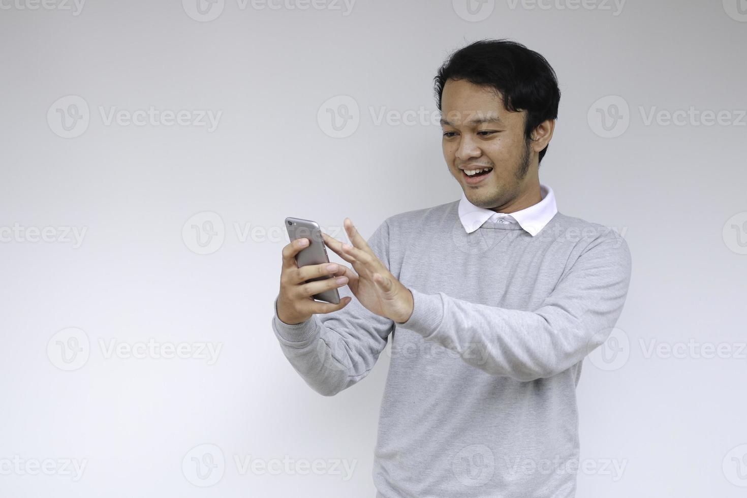 Young Asian man shocked and happy with what he see in the smartphone on isolated grey background. photo