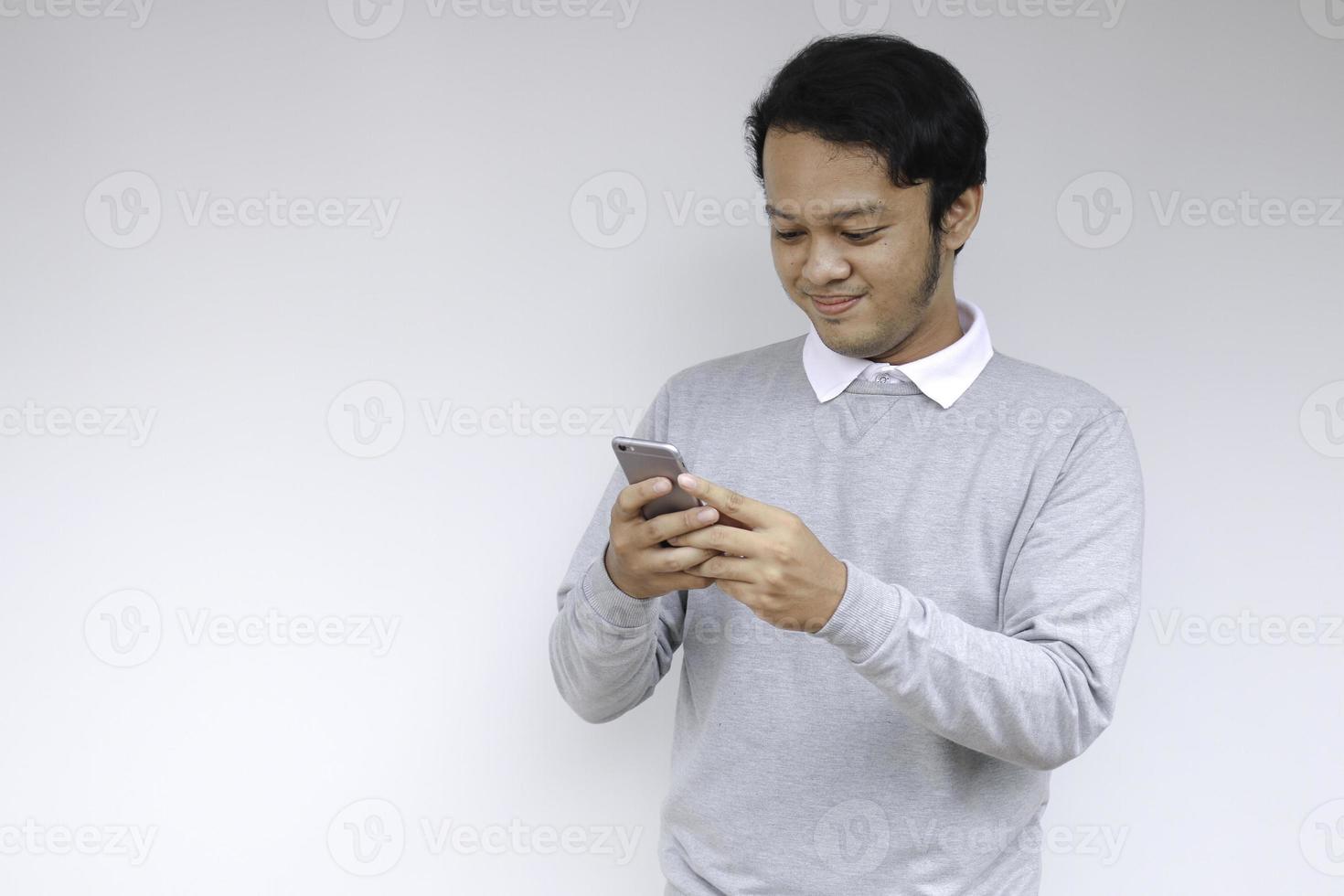 un joven asiático inteligente está feliz y sonriendo cuando usa un teléfono inteligente en el fondo del estudio foto