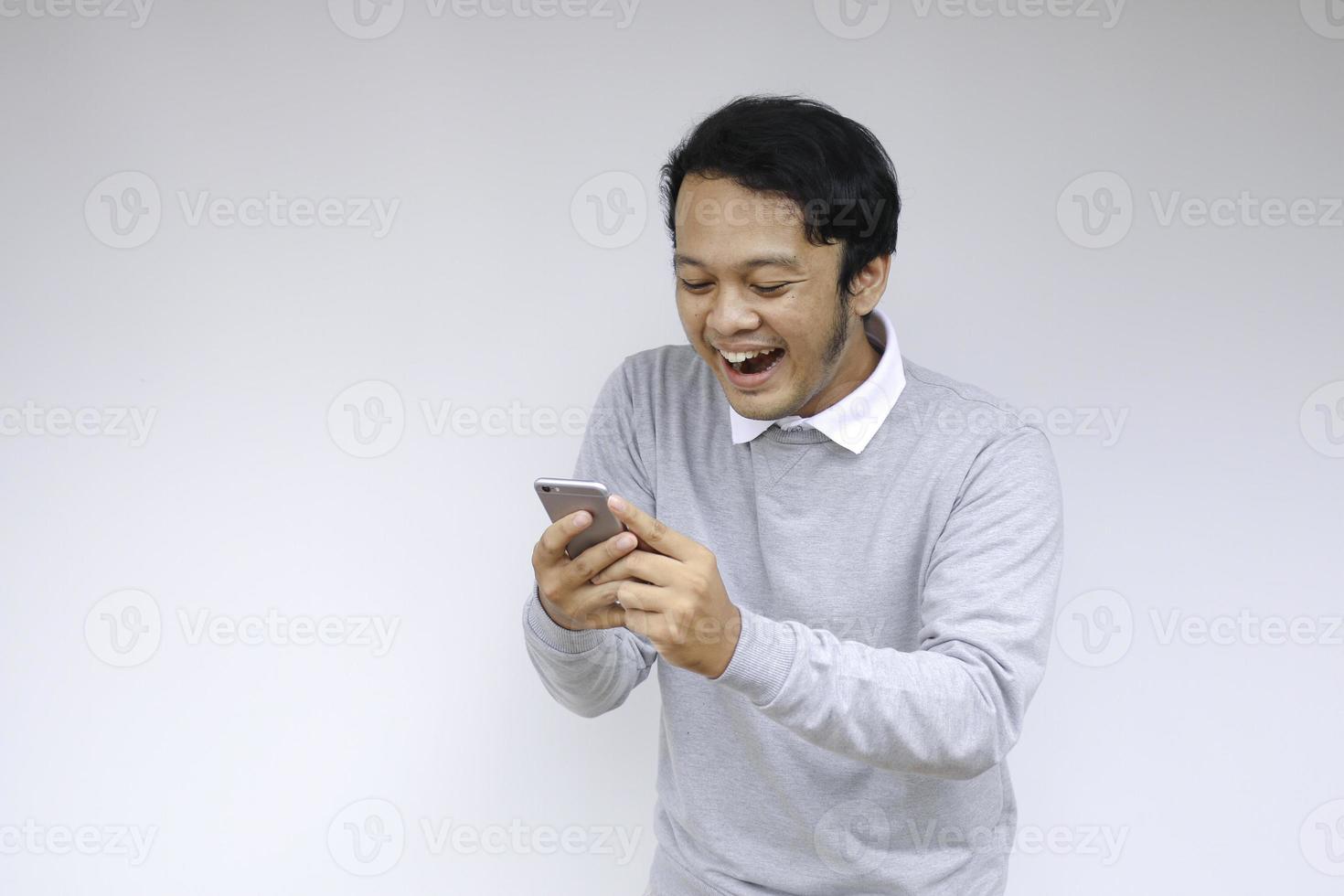 Young Asian man shocked and happy with what he see in the smartphone on isolated grey background. photo