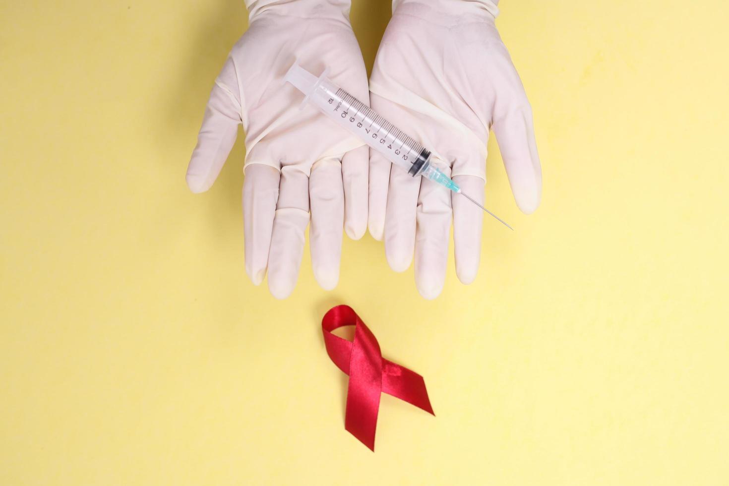red ribbon with medical gloves and syringe against HIV isolated on yellow background photo