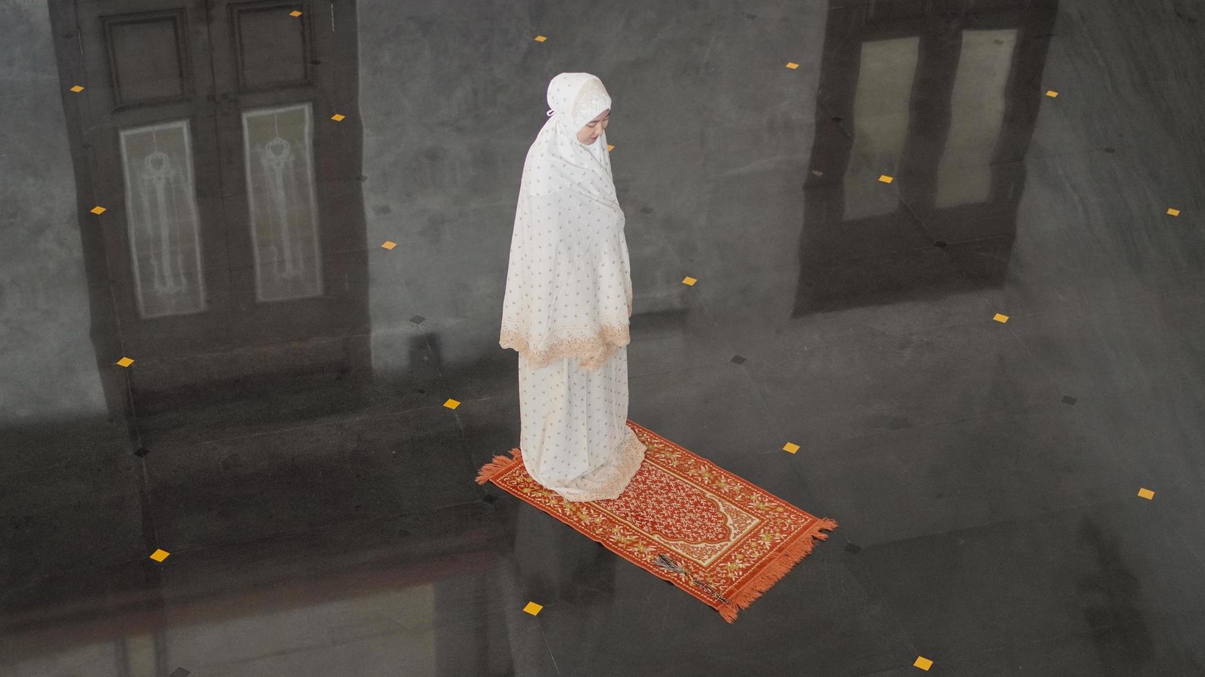 Asian Muslim woman praying alone without imam in mosque photo