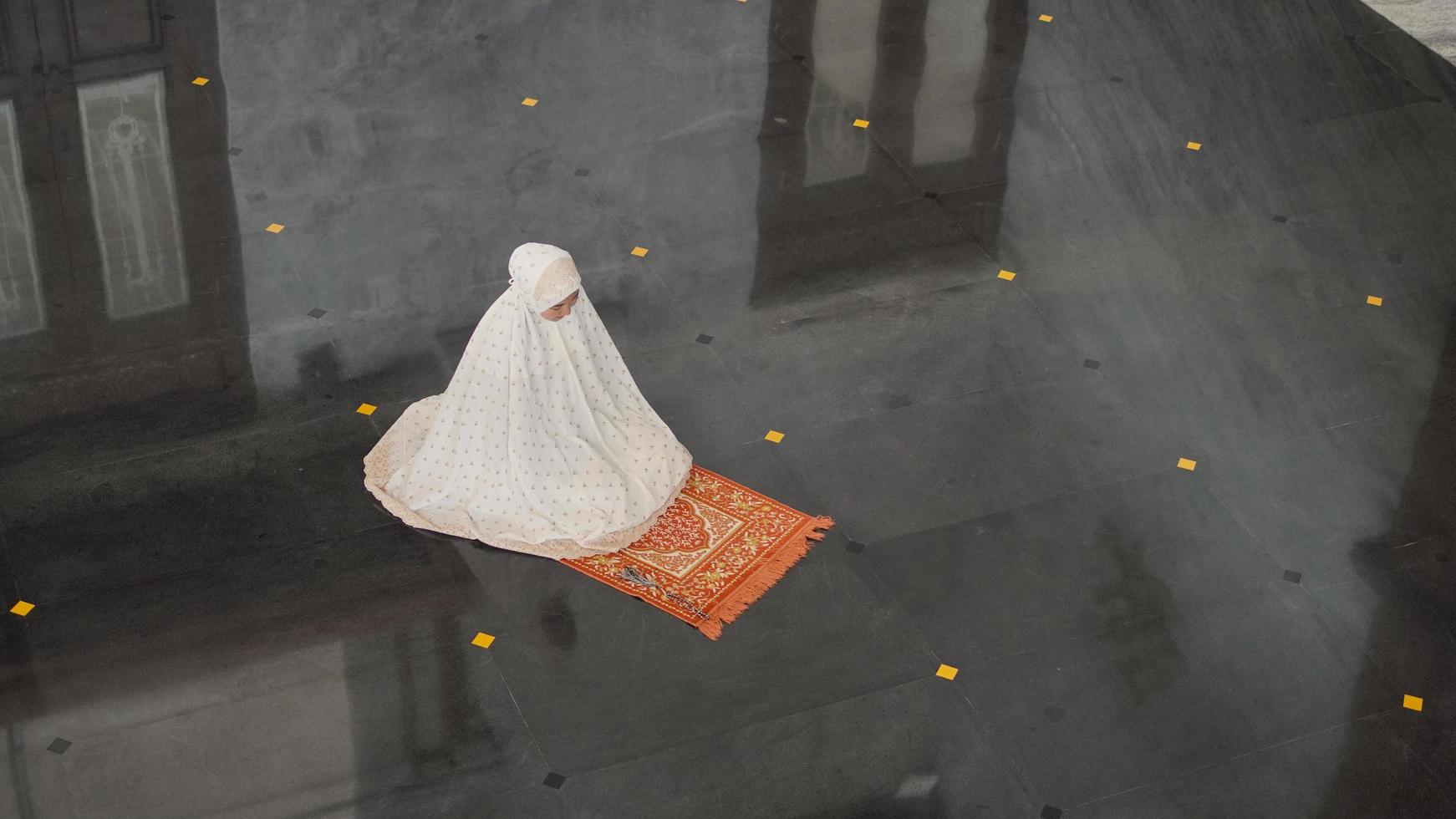 Asian Muslim woman praying alone without imam in mosque photo