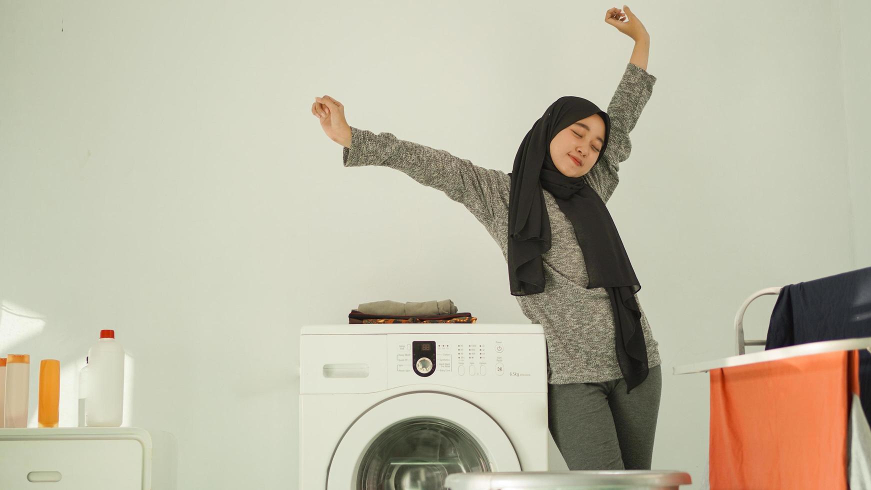 Asian woman in hijab unwinds after washing clothes at home photo