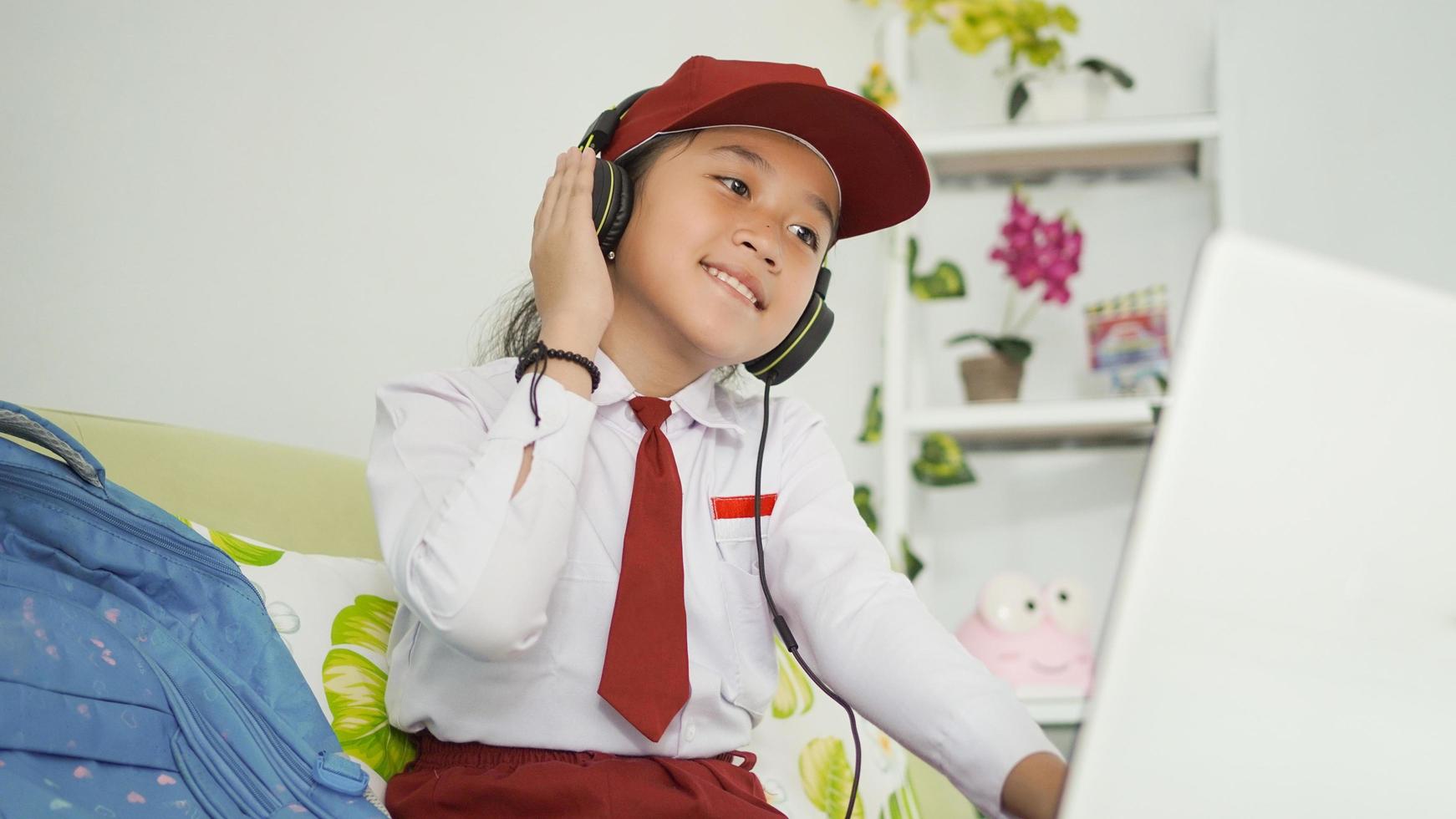 asian elementary school girl studying online at home listening using headphone photo