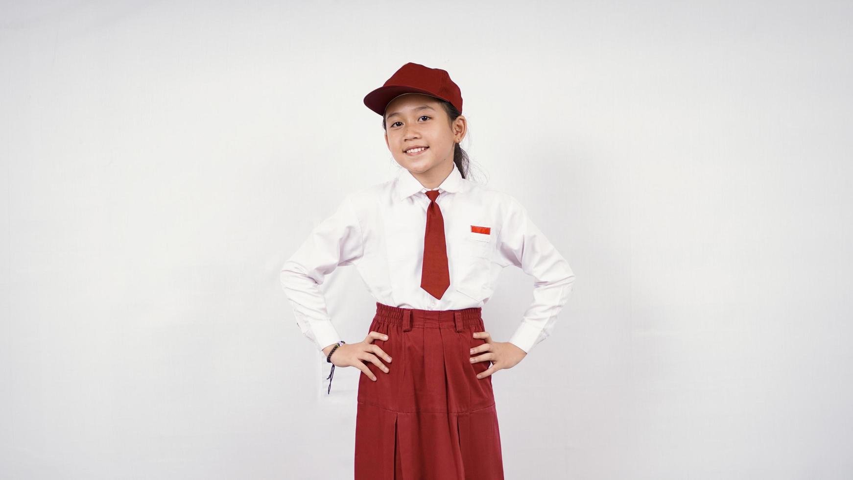 sonriente niña de la escuela primaria asiática con las manos en la cintura aislado sobre fondo blanco. foto