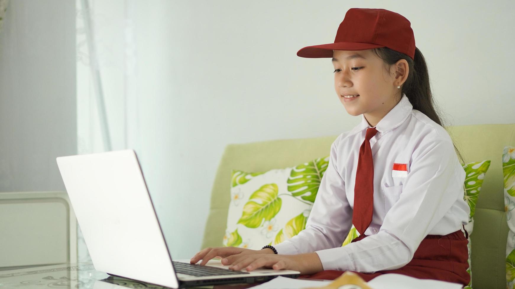 asian elementary school girl studying online from home typing on laptop photo