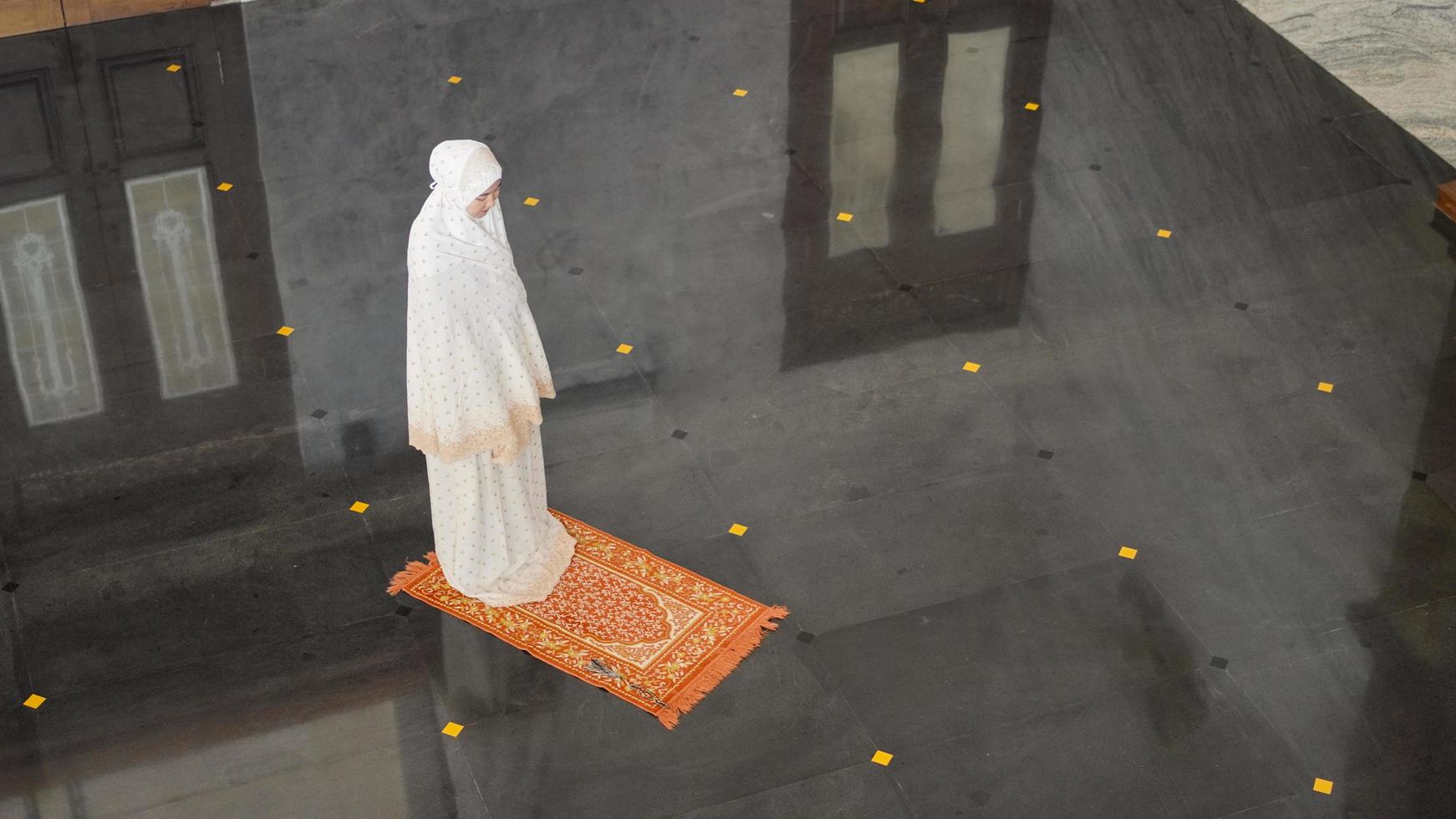 Asian Muslim woman praying alone without imam in mosque photo