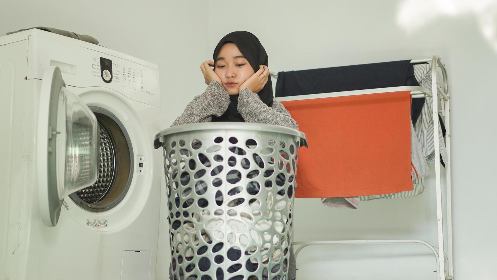 asian woman in hijab who is dirty looking at piles of dirty clothes at home photo