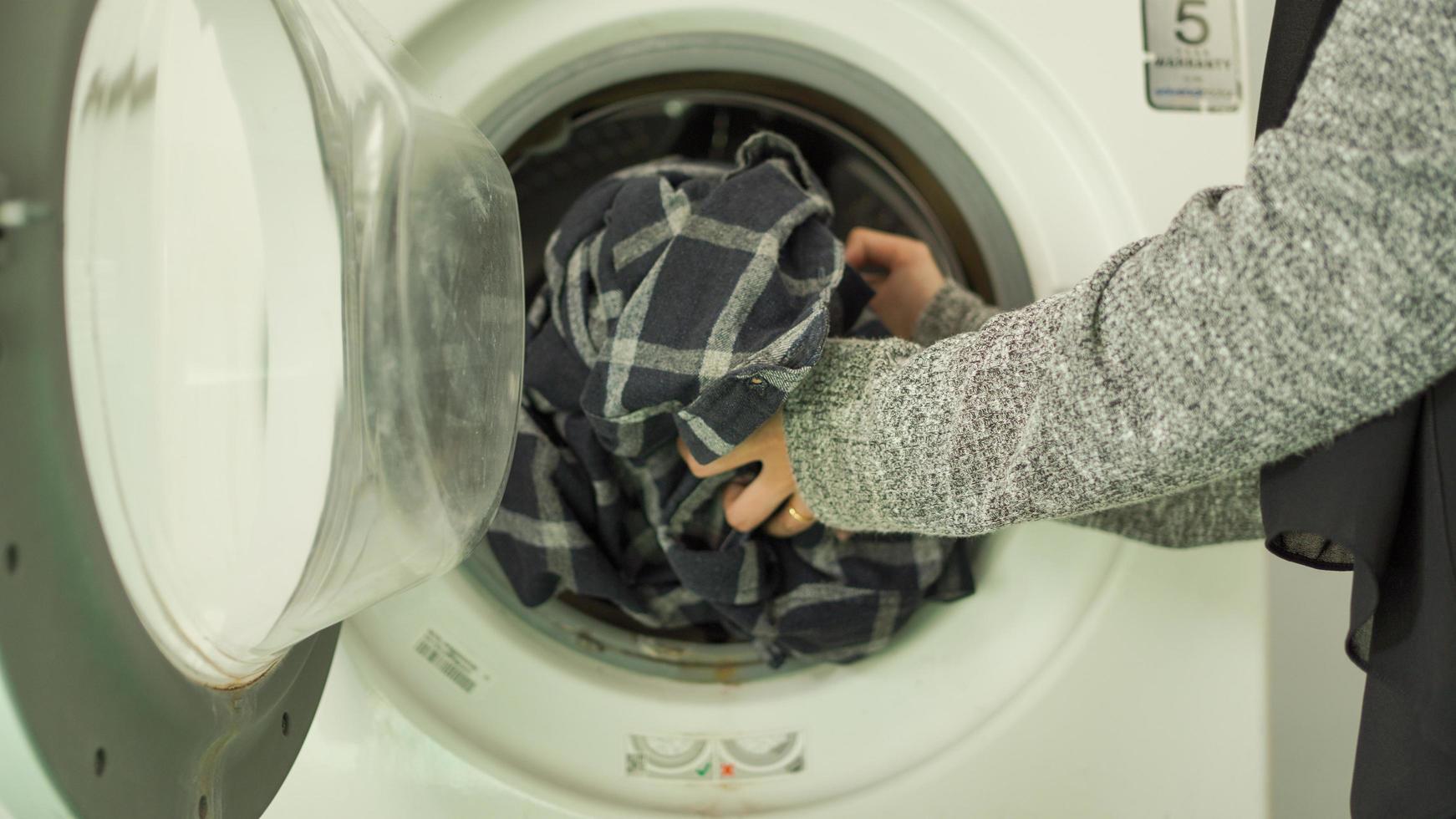 asian woman in hijab washing clothes in washing machine at home photo