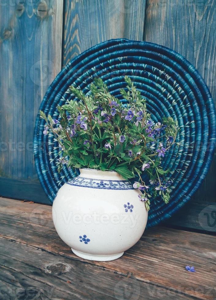 Blue field flowers in vase on wooden background photo