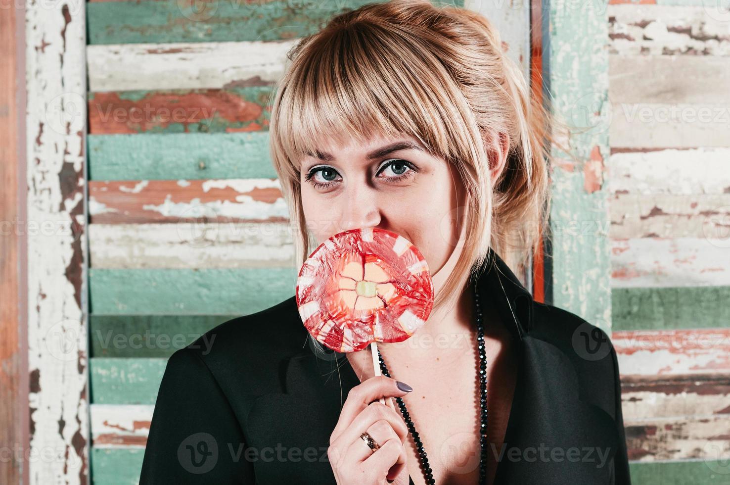 pretty blonde in black dress holding stick of red candy at her mouth photo