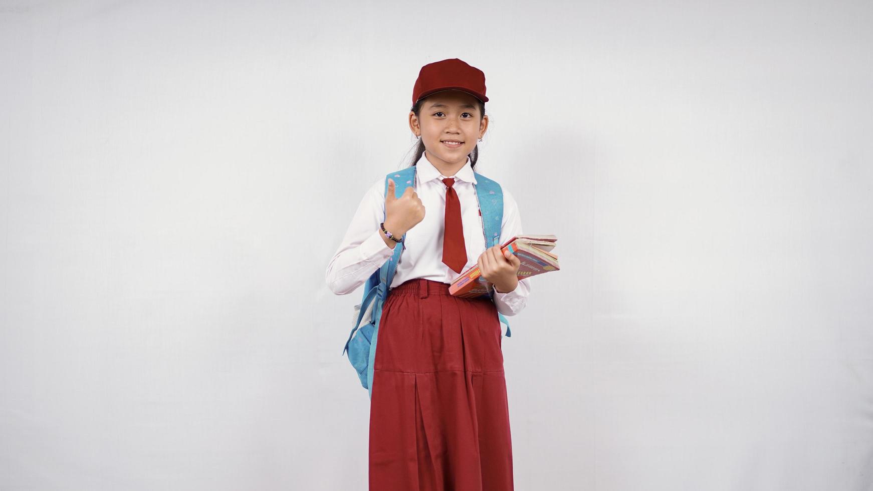 Asian elementary school girl going to leave with books and okay isolated on white background photo