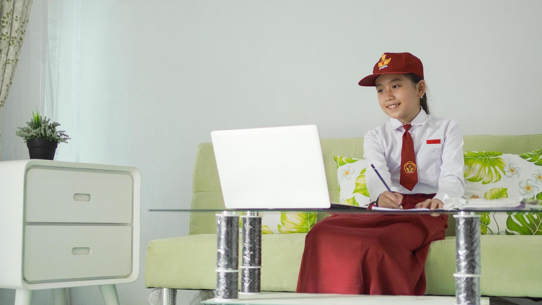 asian elementary school girl looking at laptop screen to write at home photo