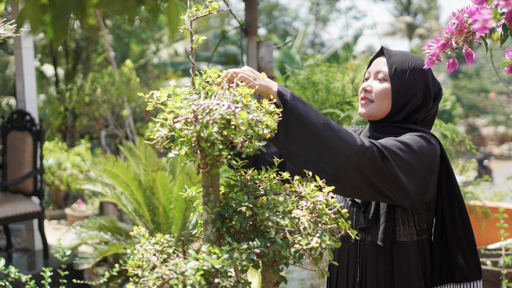 the beauty in hijab cuts the leaves in the garden photo