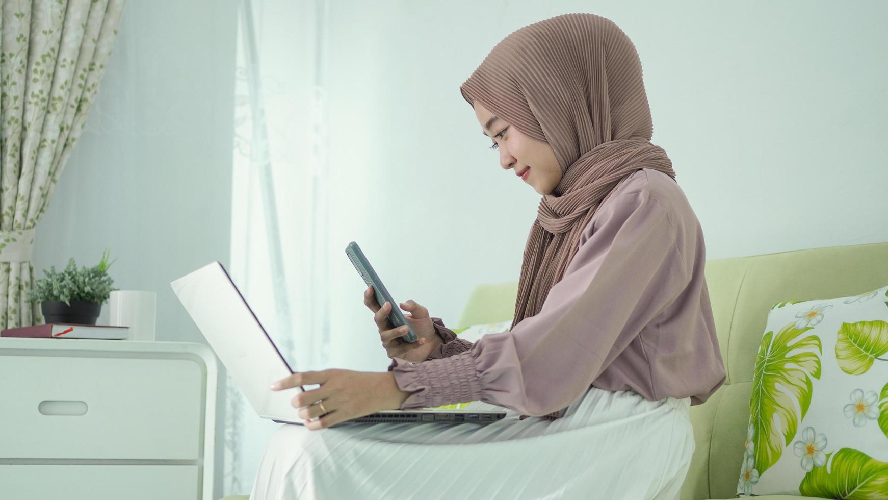 asian woman in hijab taking picture on laptop screen at home photo