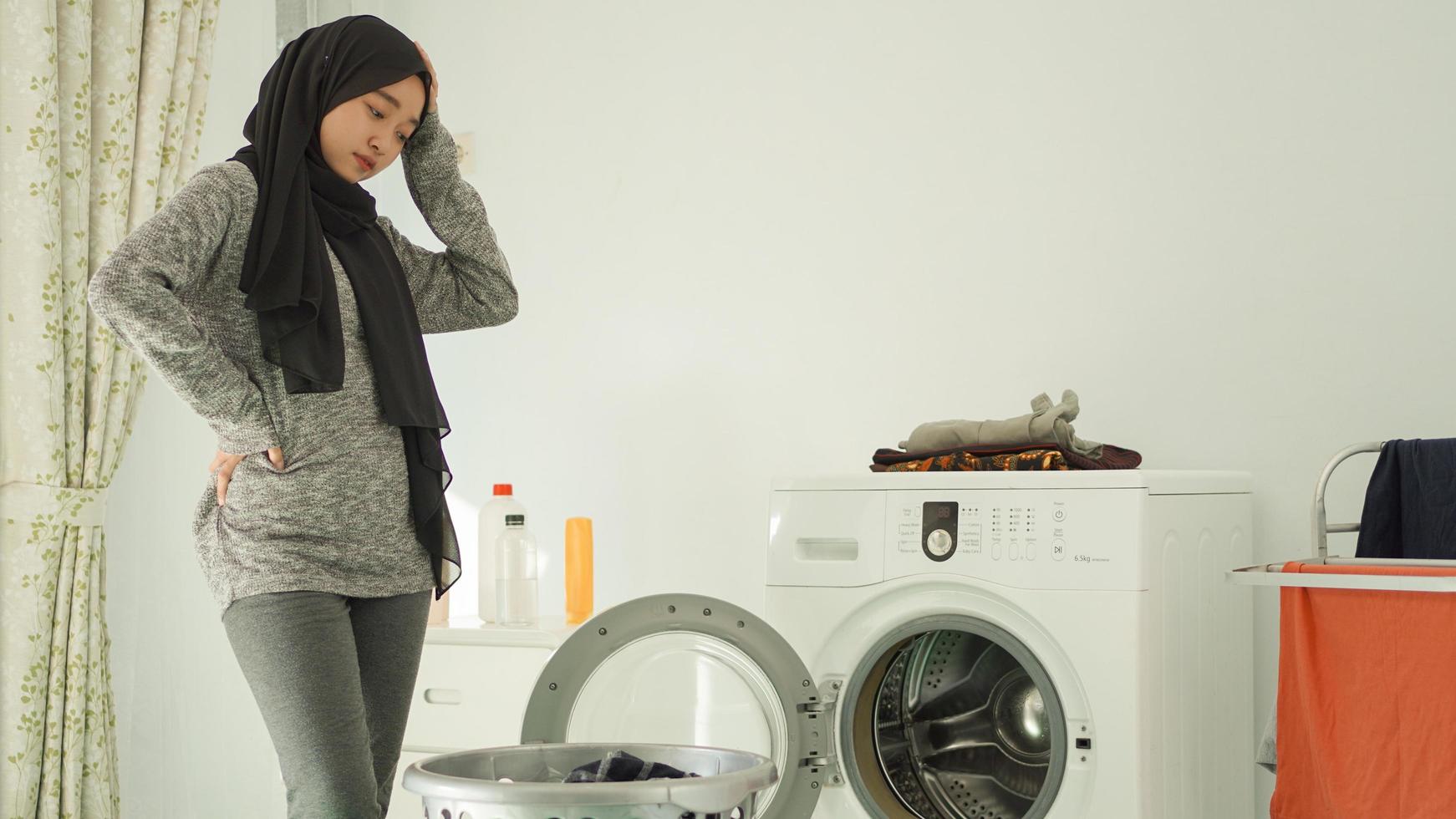 joven asiática mareada mirando la canasta de ropa sucia en casa foto