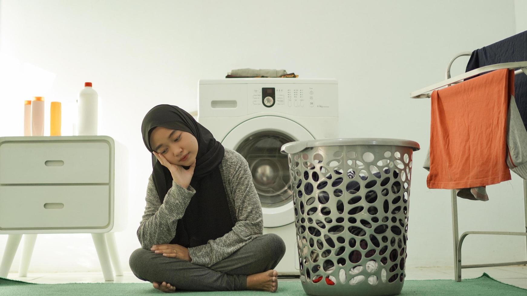 Asian woman wearing hijab is lazy to wash clothes at home photo