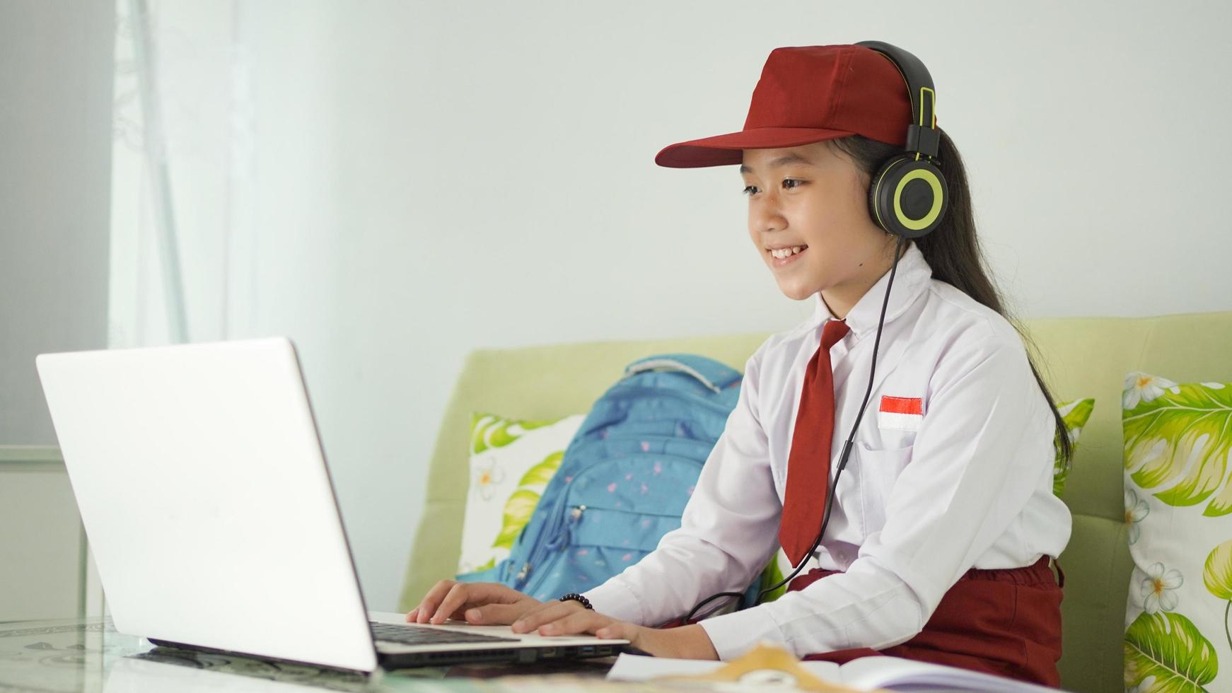 asian elementary school girl studying online using laptop at home photo