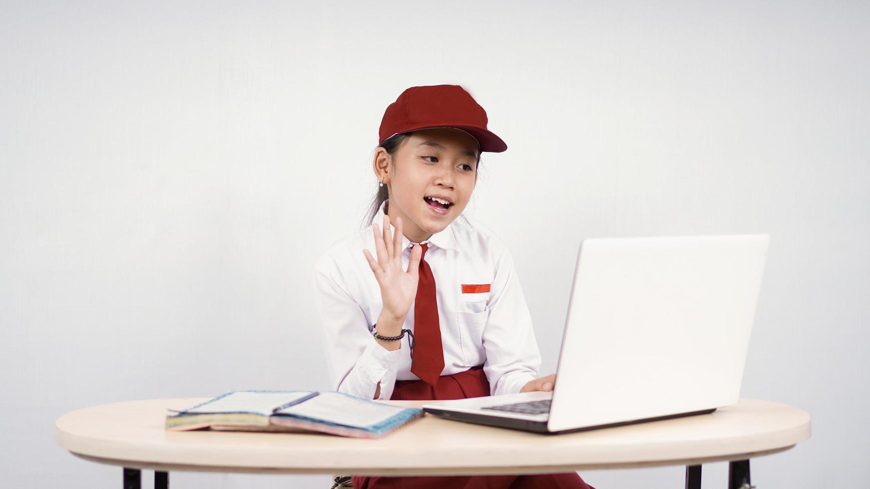 Asian elementary school girl greeting to laptop screen isolated on white background photo