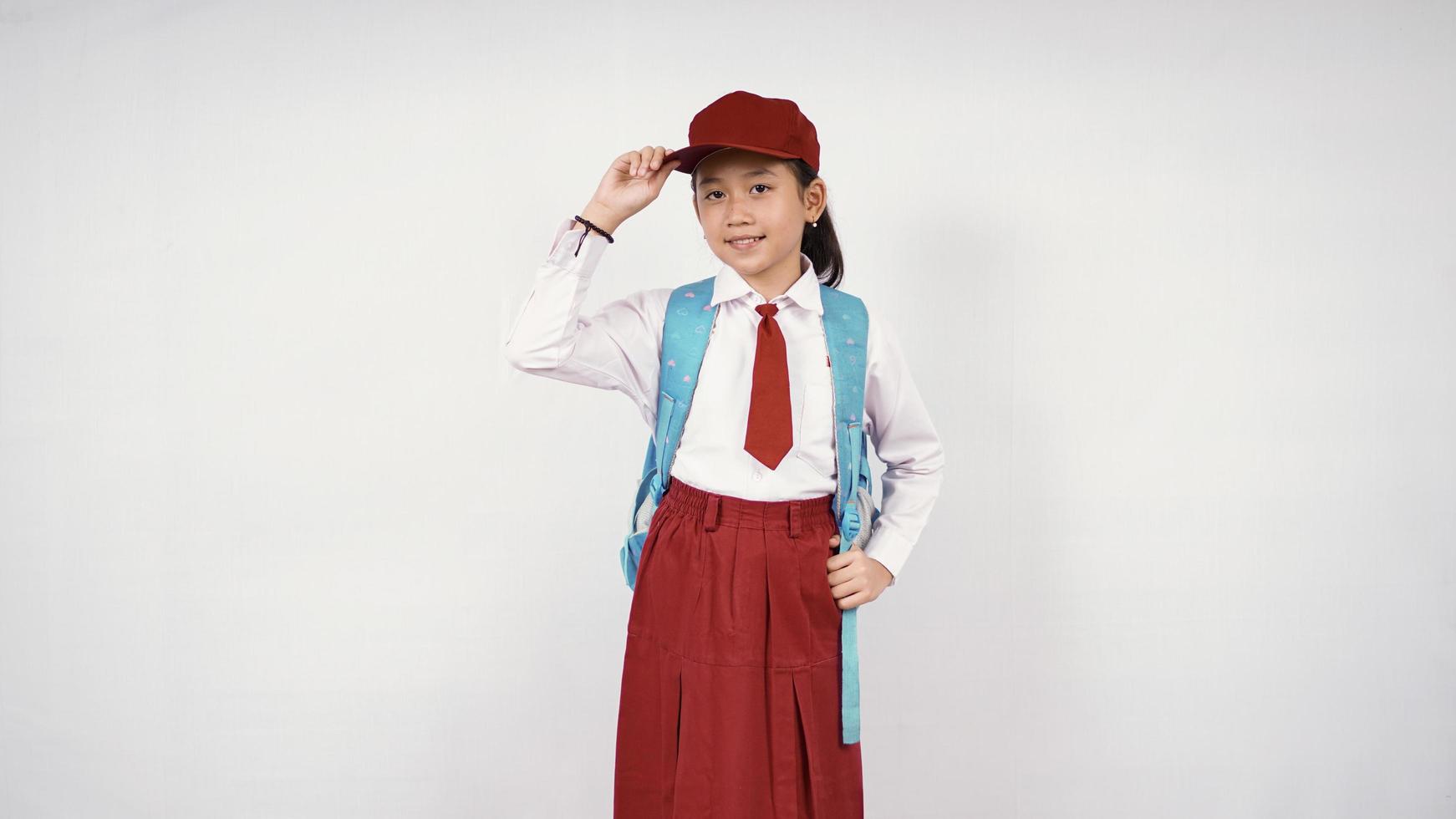 niña asiática con sombrero y mochila escolar sonriendo alegremente con fondo blanco aislado foto