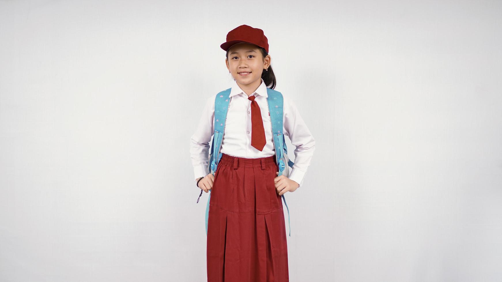 niña asiática con sombrero y mochila escolar sonriendo alegremente con fondo blanco aislado foto