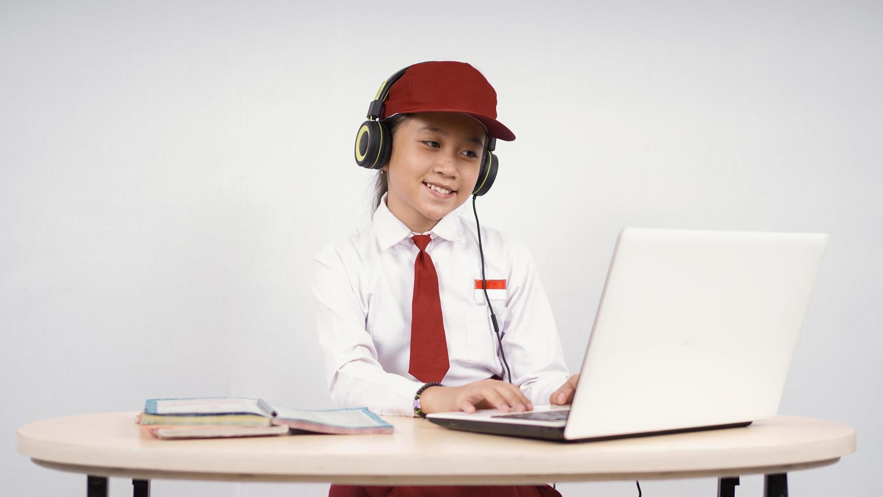 Elementary school asian girl listening on headphones while studying isolated on white background photo