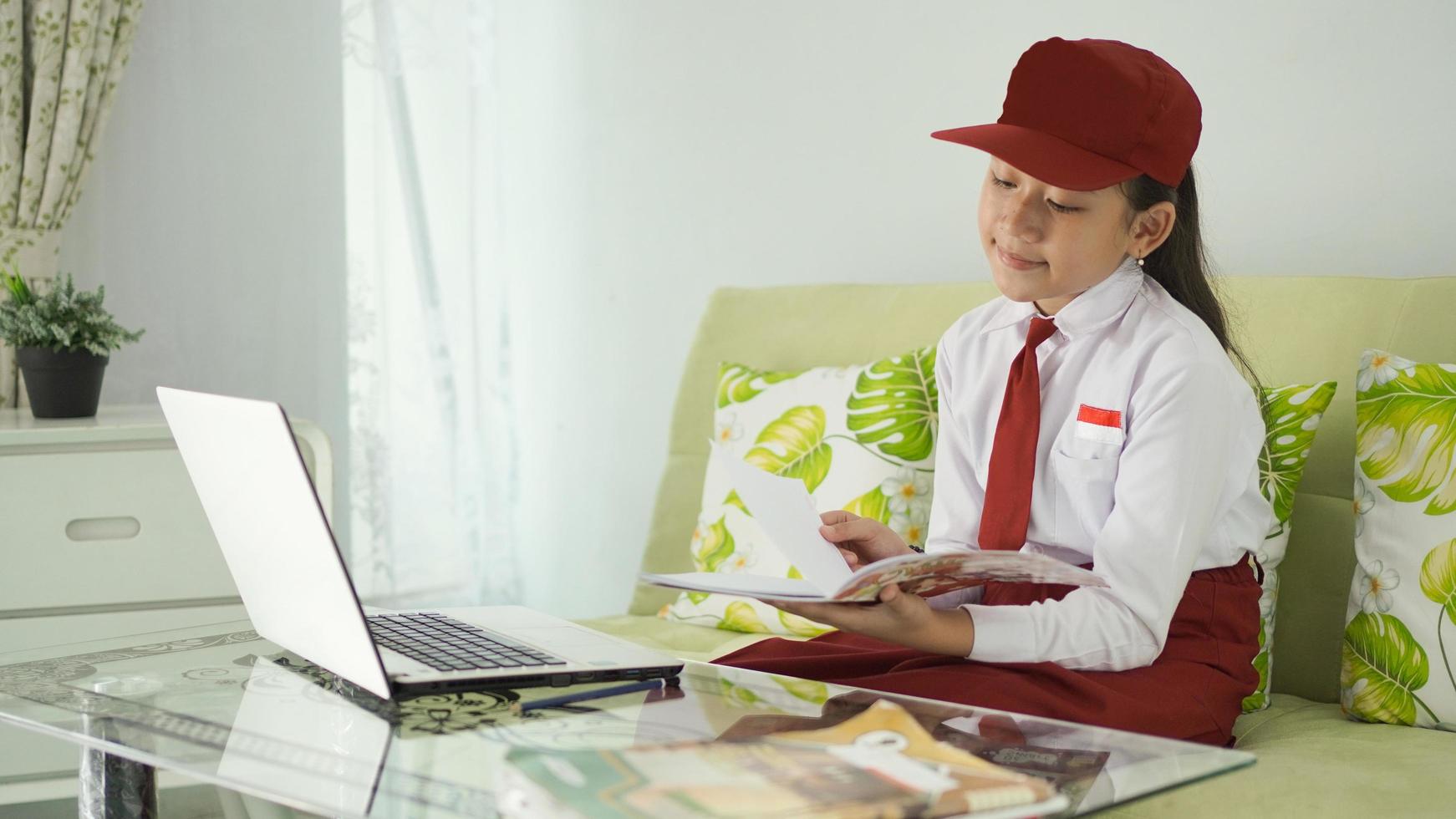 asian elementary school girl studying online from home reading books happily photo