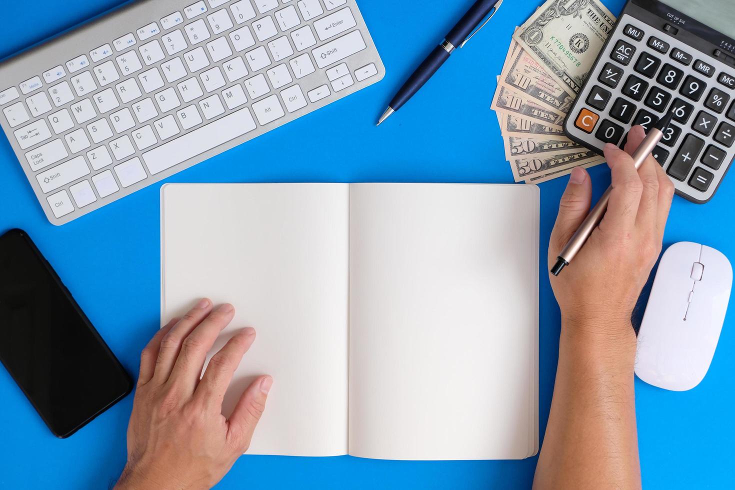 Blank notebook with pen is placed on an office desk table with computer tools and a range of materials. finance and banking background, flat lay, top view photo