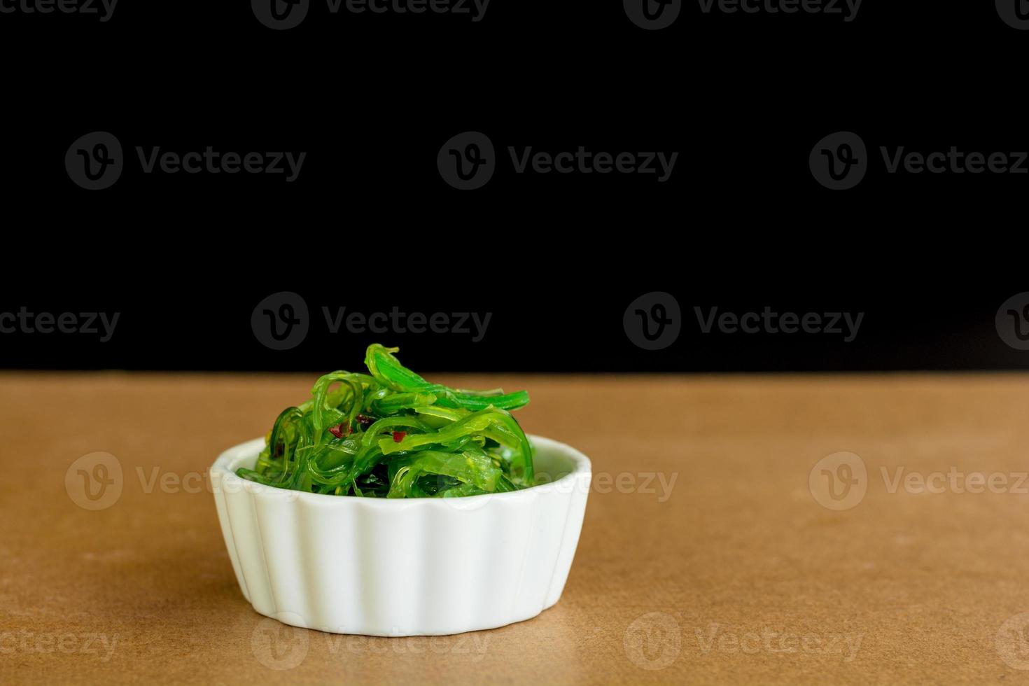 Japanese food concept. Fresh seaweed salad with sesame seeds in white bowl on black background. photo