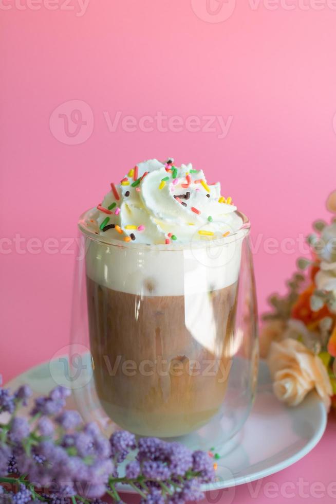 Ice coffee with a layer of milk and whipping cream with color sugar topping on pink background. Beverage and drink at the party concept. photo