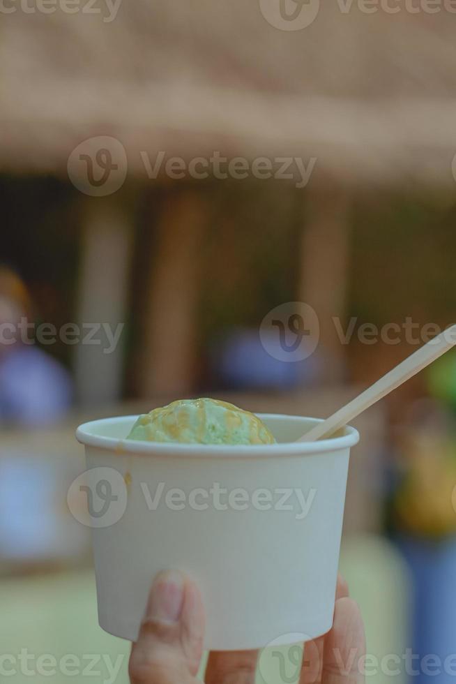 Delicious avocado ice cream in white paper bowl on hand with wooden spoon with copy space for your text. Reduce plastic concept. photo