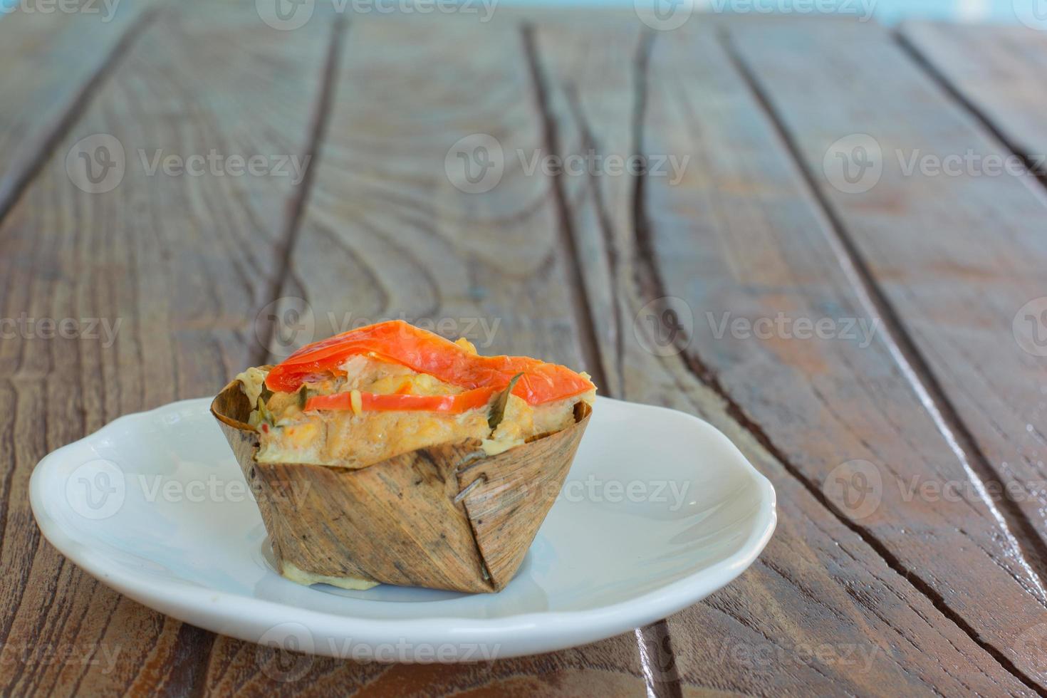 Thai steamed seafood curry in cup made from dry banana leave on wooden table and red chilli topping. Delicious Thai food. photo