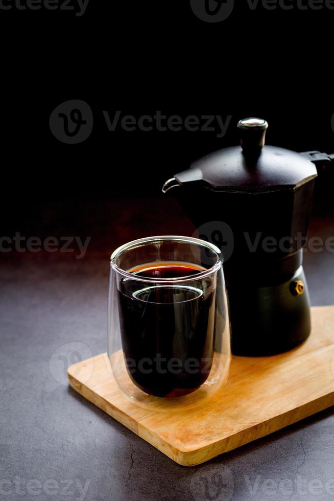 Espresso or black coffee and moka pot on wooden chopping board and dark table. Benefit of coffee concept. photo