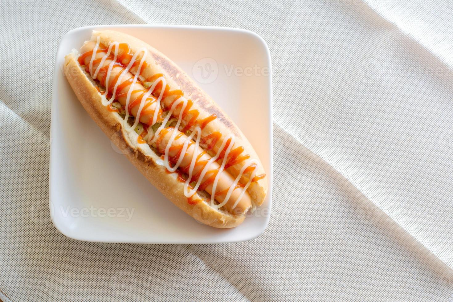 Top view Hot dog with bun and ketchup, mayonnaise on white plate. Sausage sandwich for lunch. Fast food concept. photo