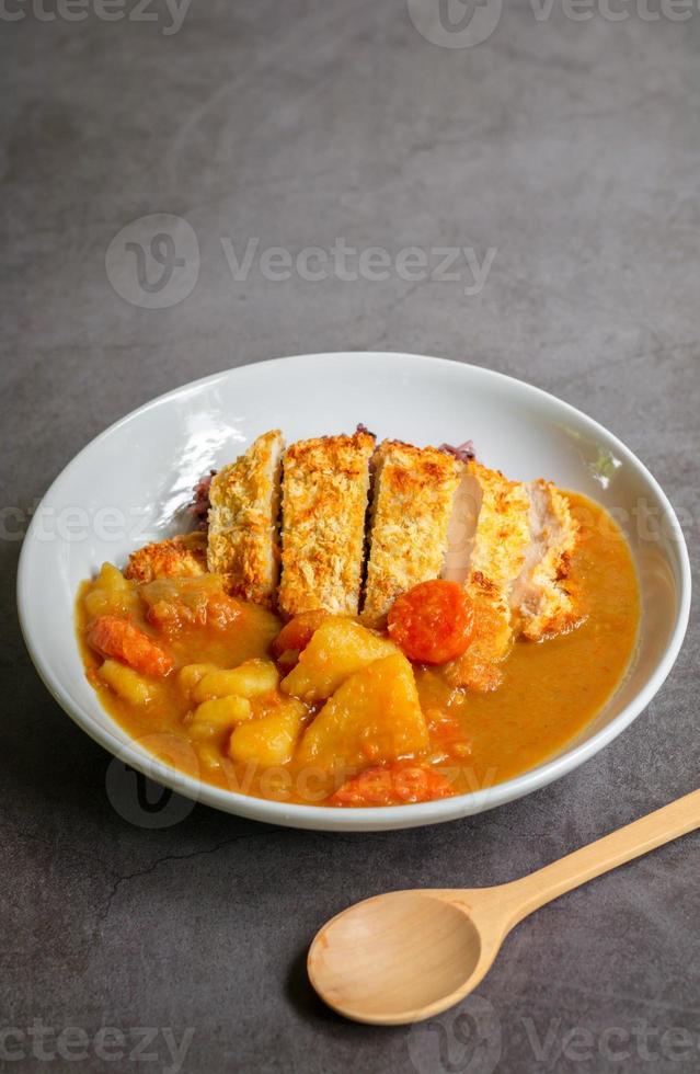 Japanese curry with rice, carrot, potato and deep fries chicken in white dish on table. photo