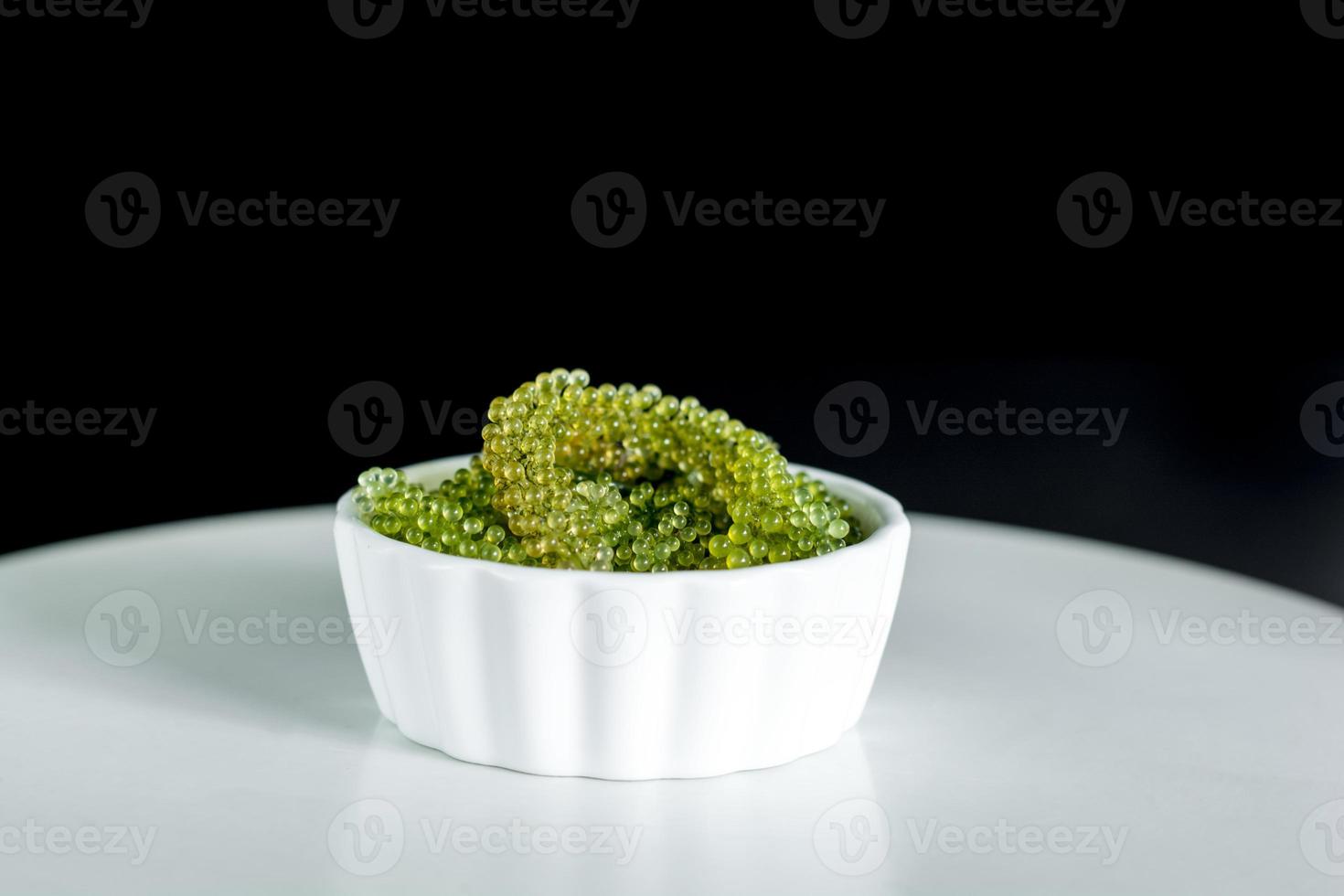 Fresh sea grapes or caviar seaweed in white bowl on black background. Healthy food concept. photo