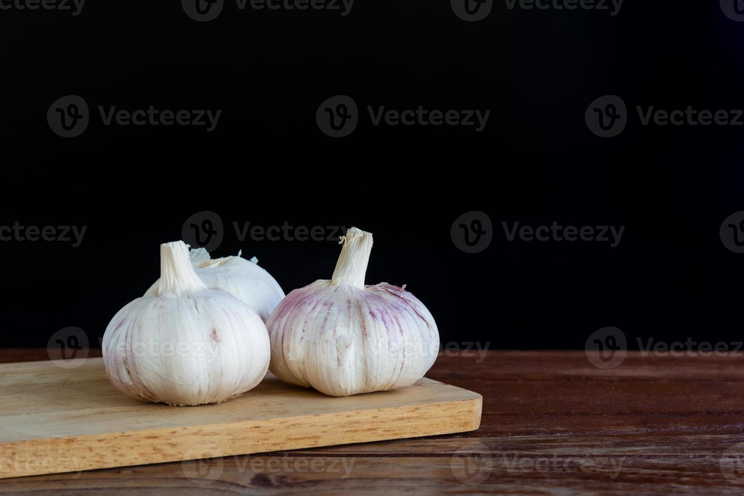 Group of garlic on chopping board and wooden table with black background. Copy space for your text. photo