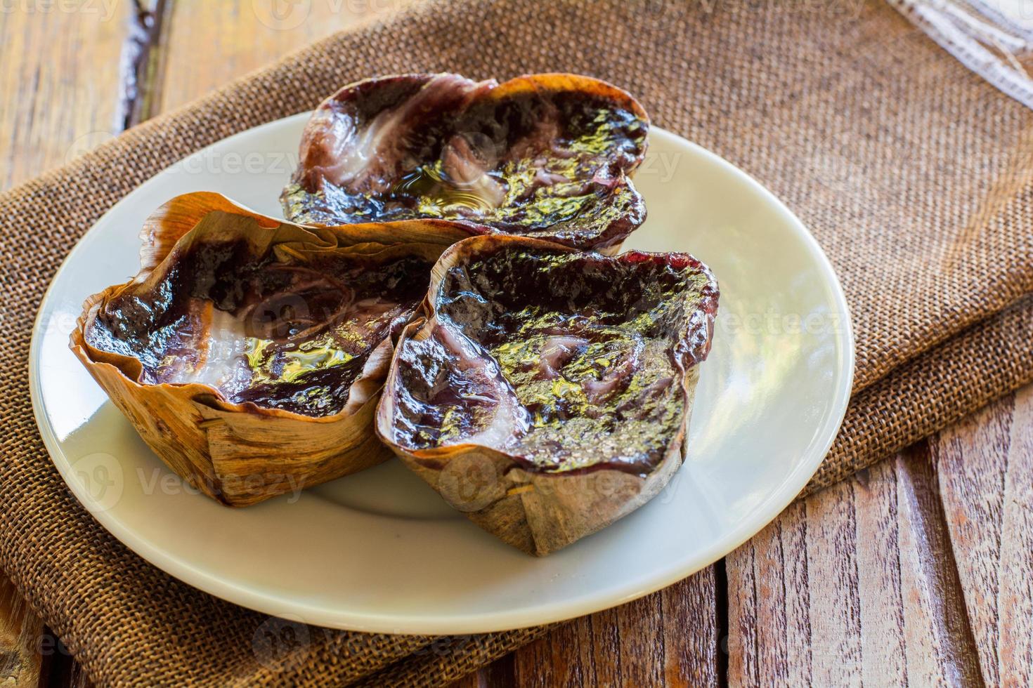 Black sticky rice cake Nian Gao in dried banana leave cup on white plate and wooden table. Traditional snack in Chinese new year. photo