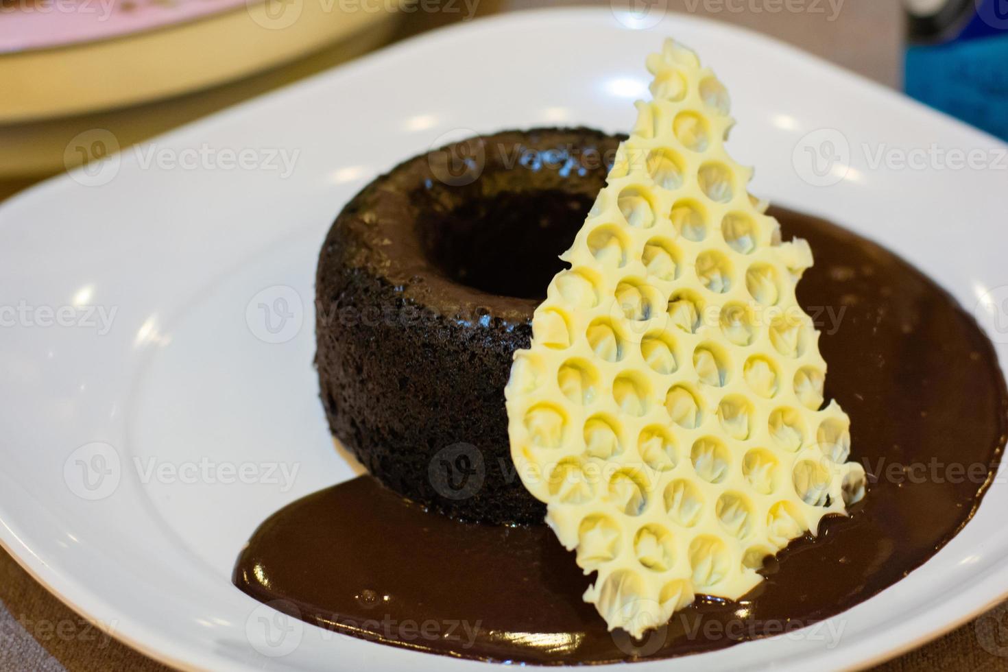 pastel redondo de chocolate oscuro con salsa de chocolate y un punto de chocolate blanco decorado con un plato blanco en la cafetería. deliciosa panadería dulce. foto