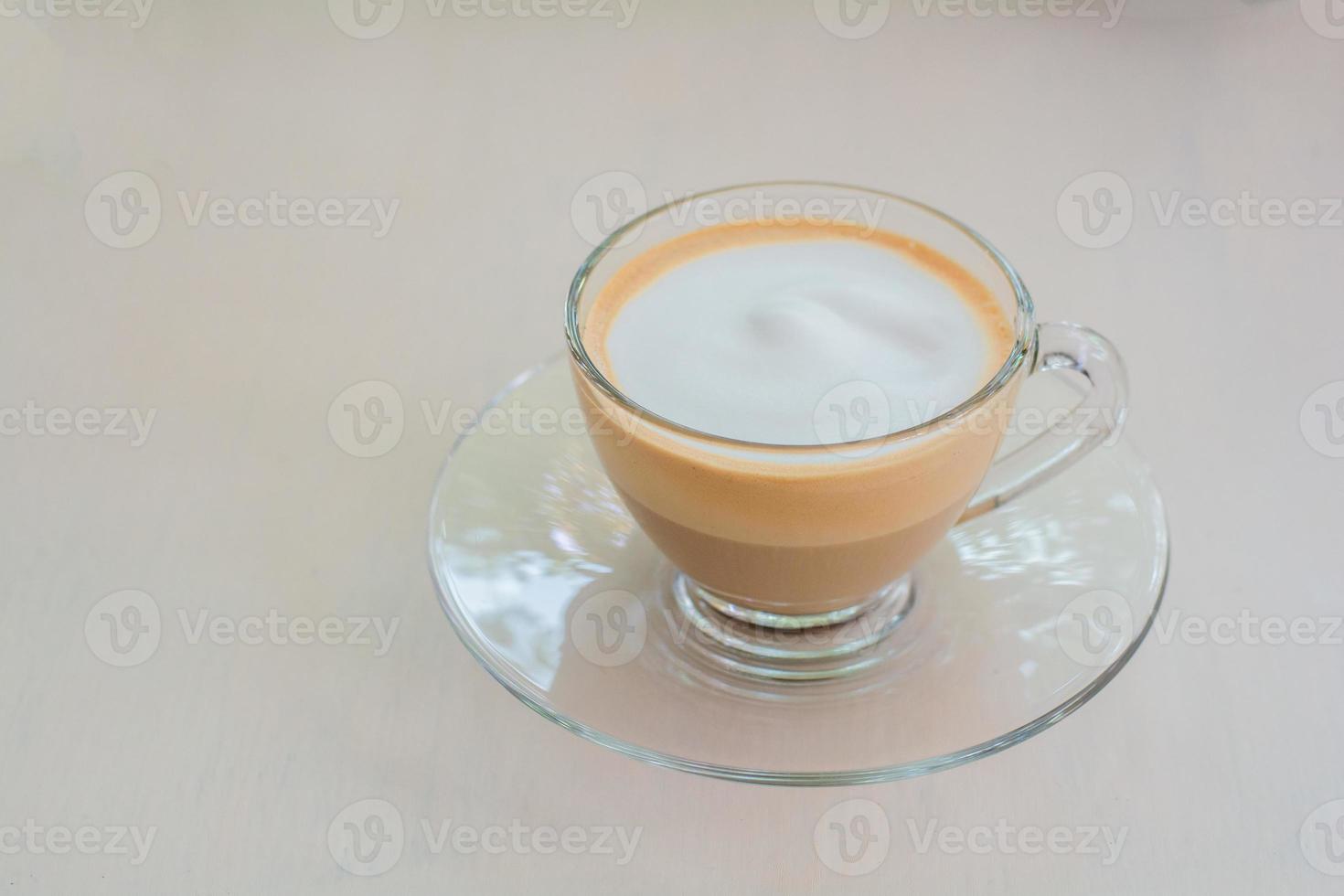 Layer of hot cappuccino coffee and milk froth in clear cup on wooden table in coffee shop. photo