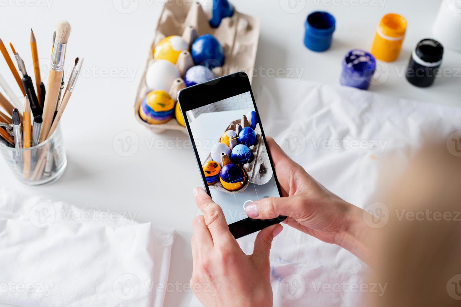 Woman coloring Easter eggs in the kitchen, taking photo on mobile