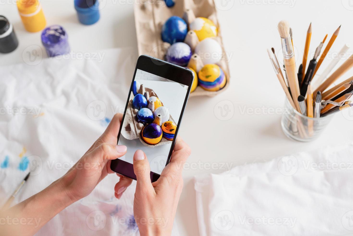 mujer coloreando huevos de pascua en la cocina, tomando fotos en el móvil