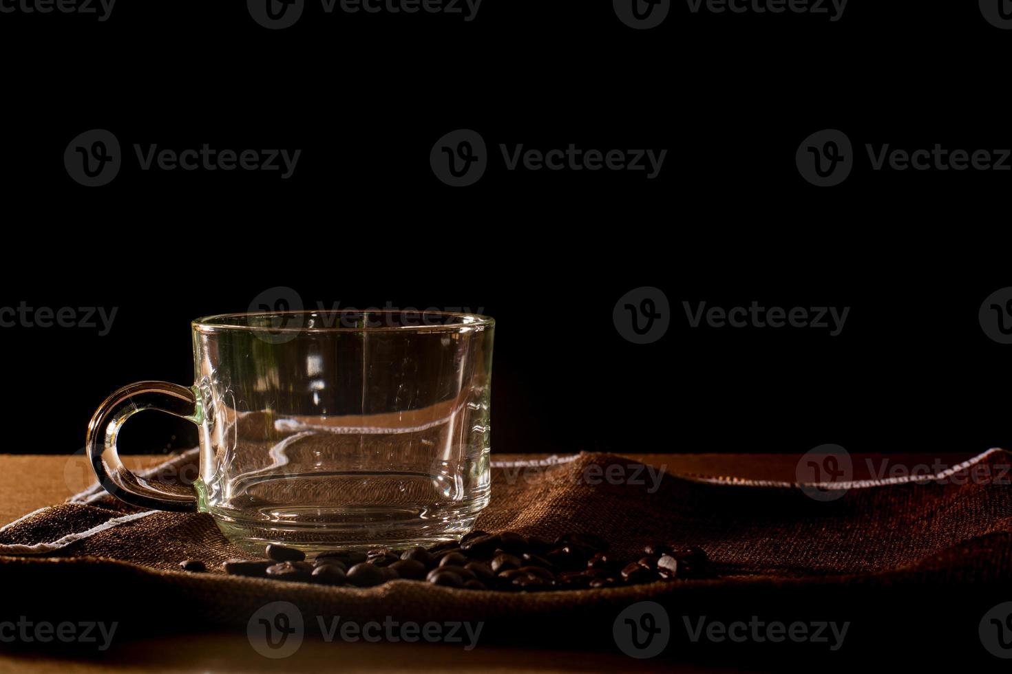 Empty cup and group of coffee beans on brown table cloth with black background with copy space for your text. Benefits of coffee concept. photo