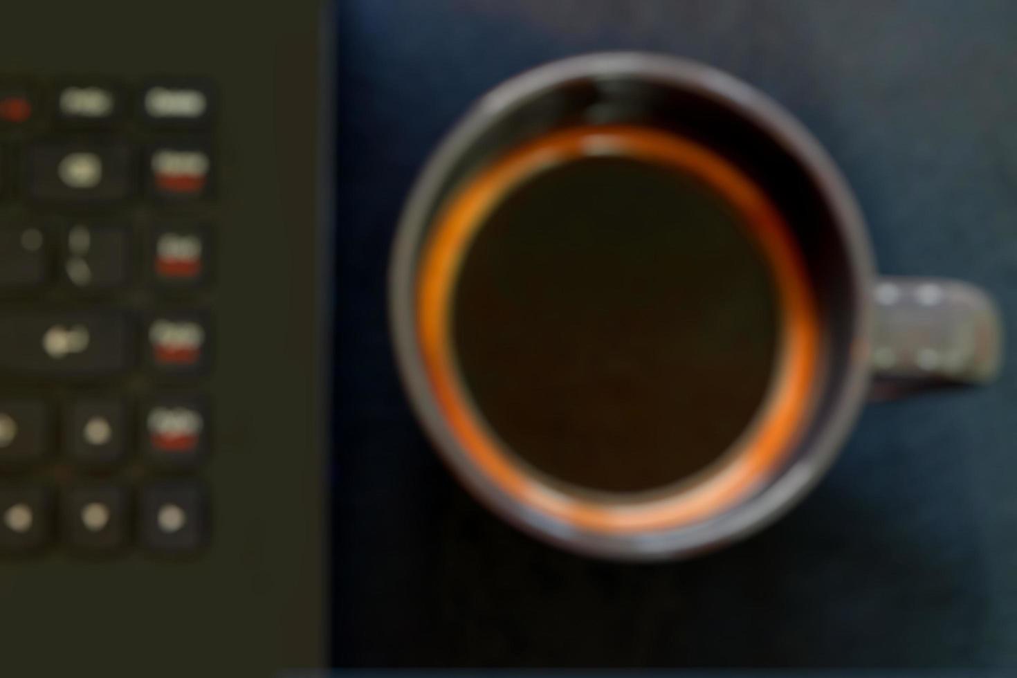 blur of coffee cup and part of computer keyboard on dark color table photo