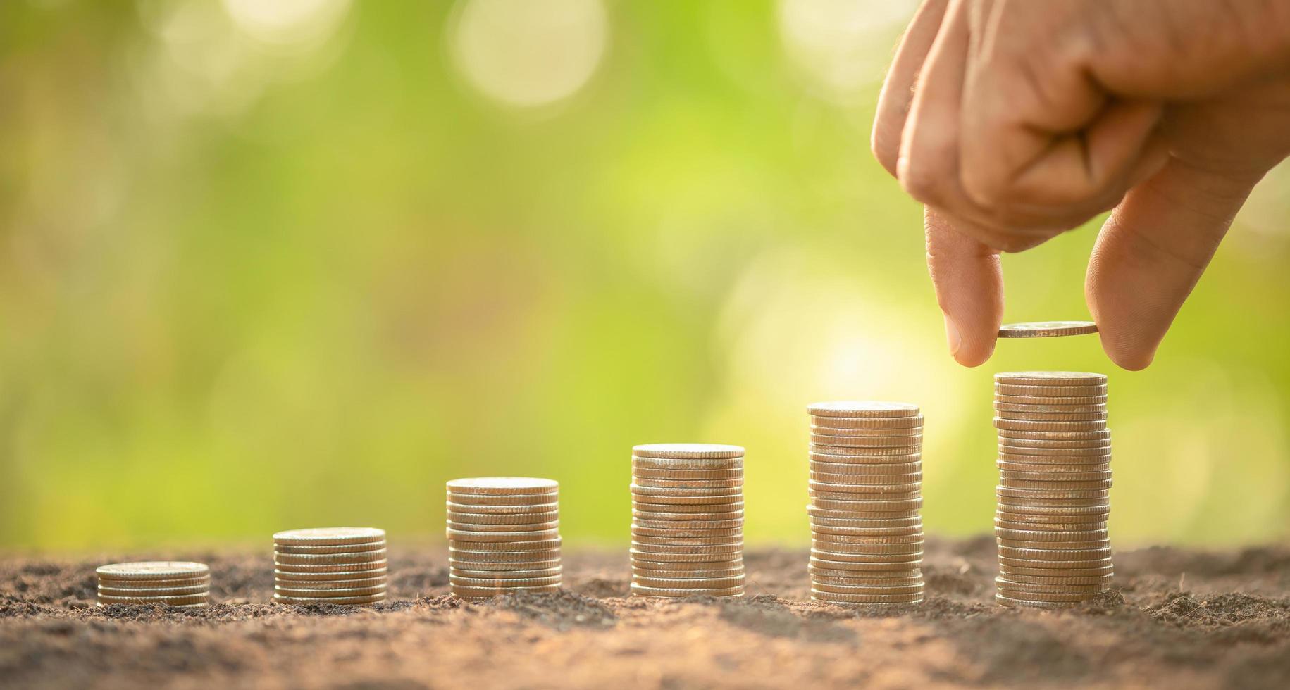 Hand putting coins in stack on wooden plank with green blur background. Money, Finance or Savings concept photo